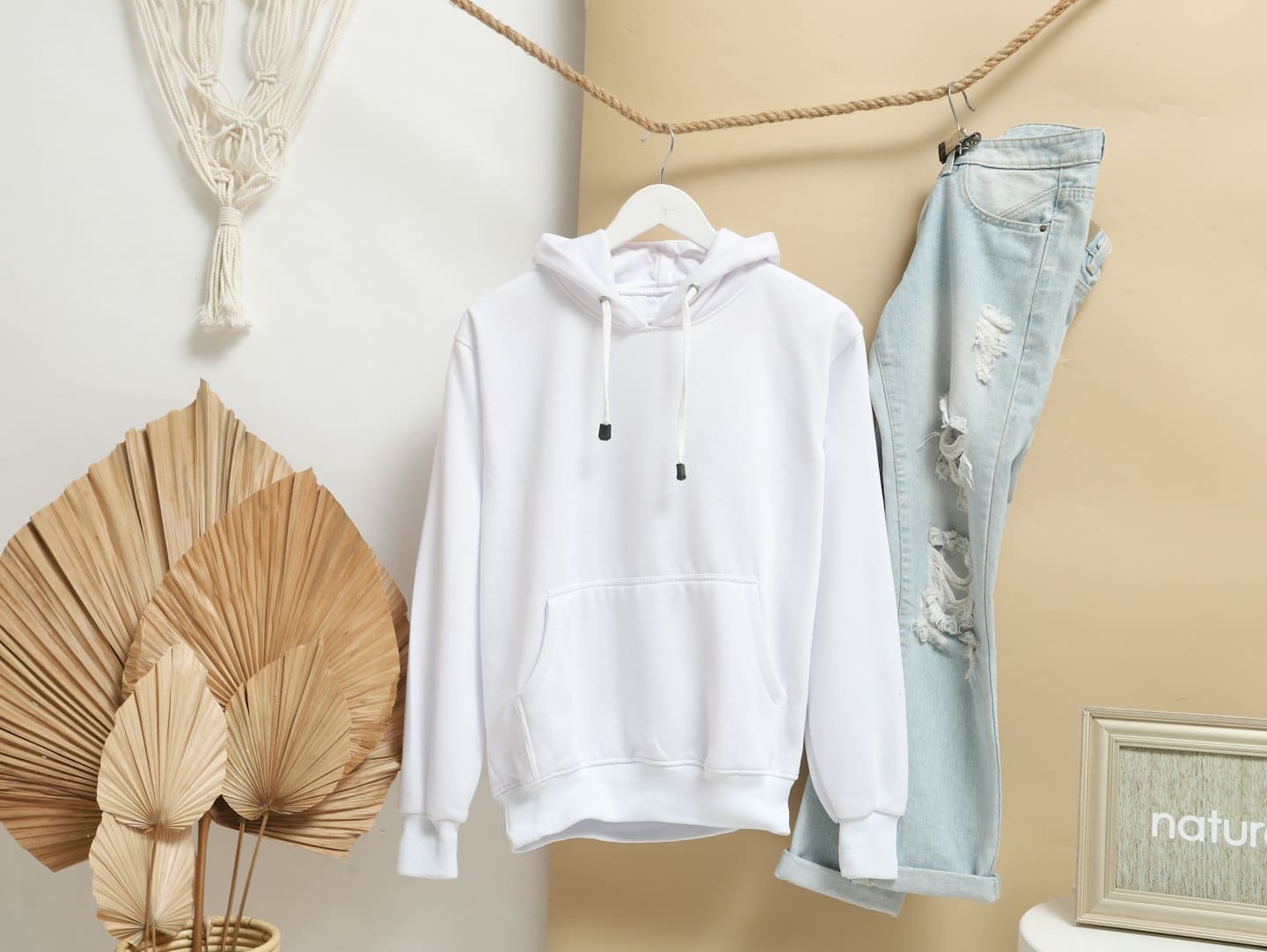 Weiße Kapuzenjacke und blaue Jeans hängen an einem Seil vor einer Wand.