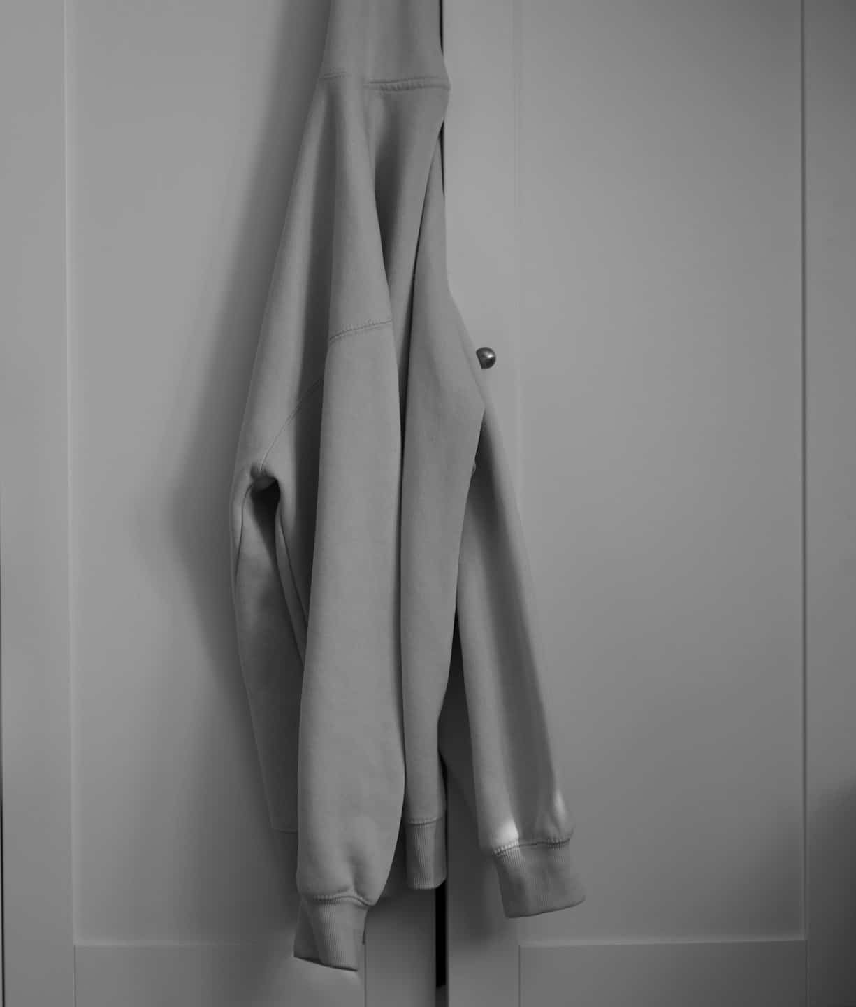 Ein cremefarbener Hoodie hängt an einem Kleiderschrankknauf.
